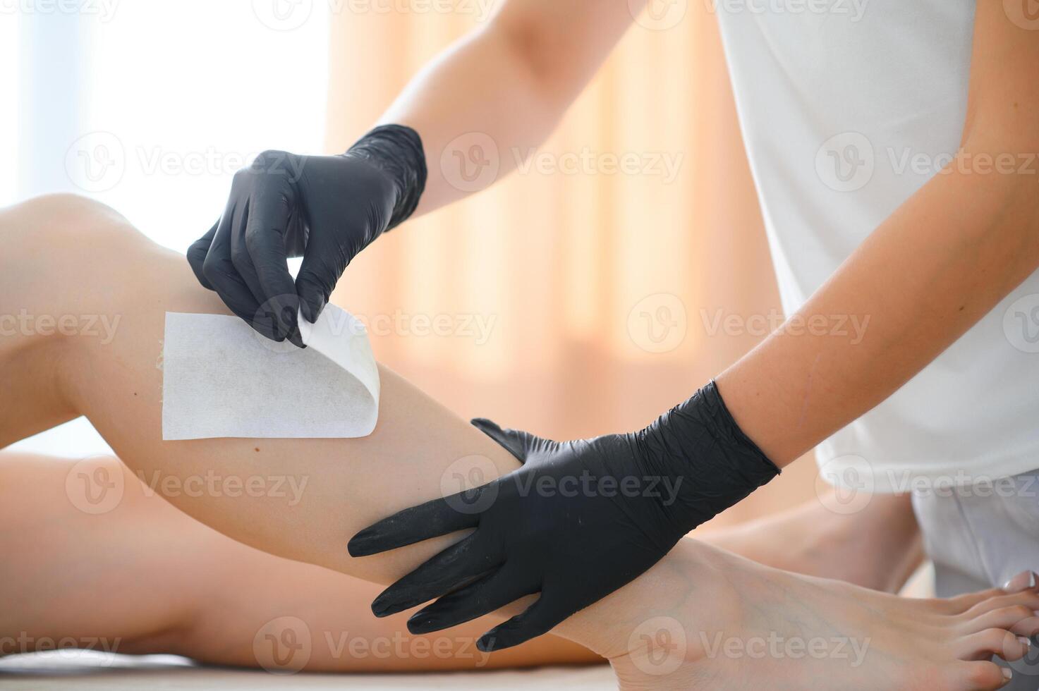 Beautician waxing female legs in spa center photo