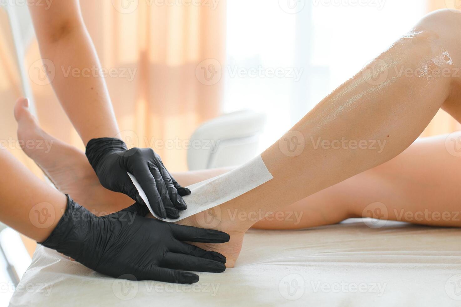 Beautician waxing female legs in spa center photo