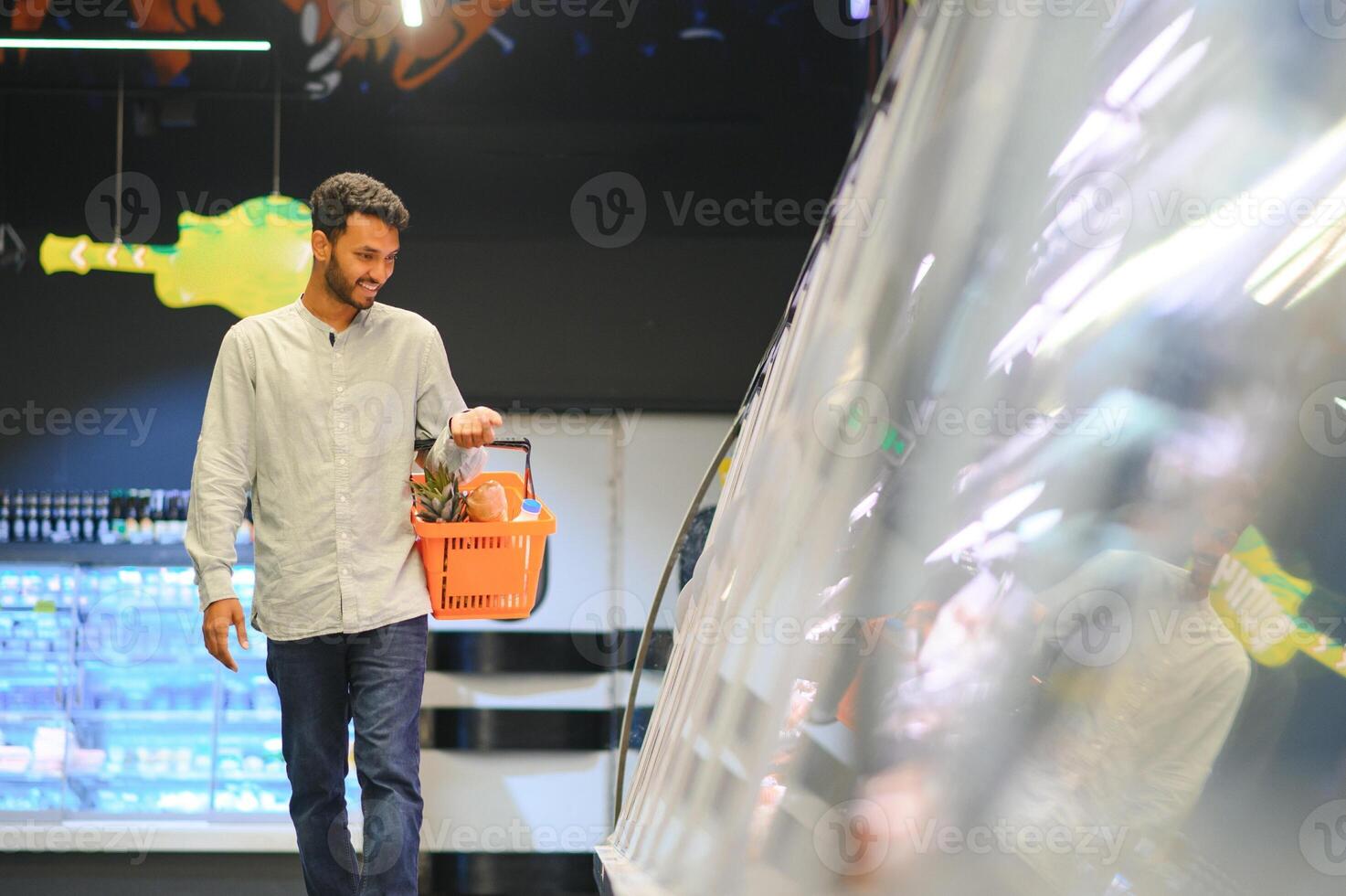 Portrait of happy Indian man standing in front of the product counter in a grocery store. Man buying grocery for home in supermarket. photo