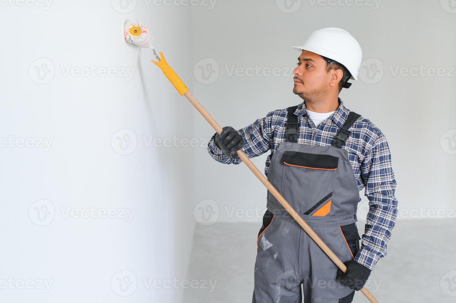 An Indian apartment repair worker paints a white wall with a roller. photo