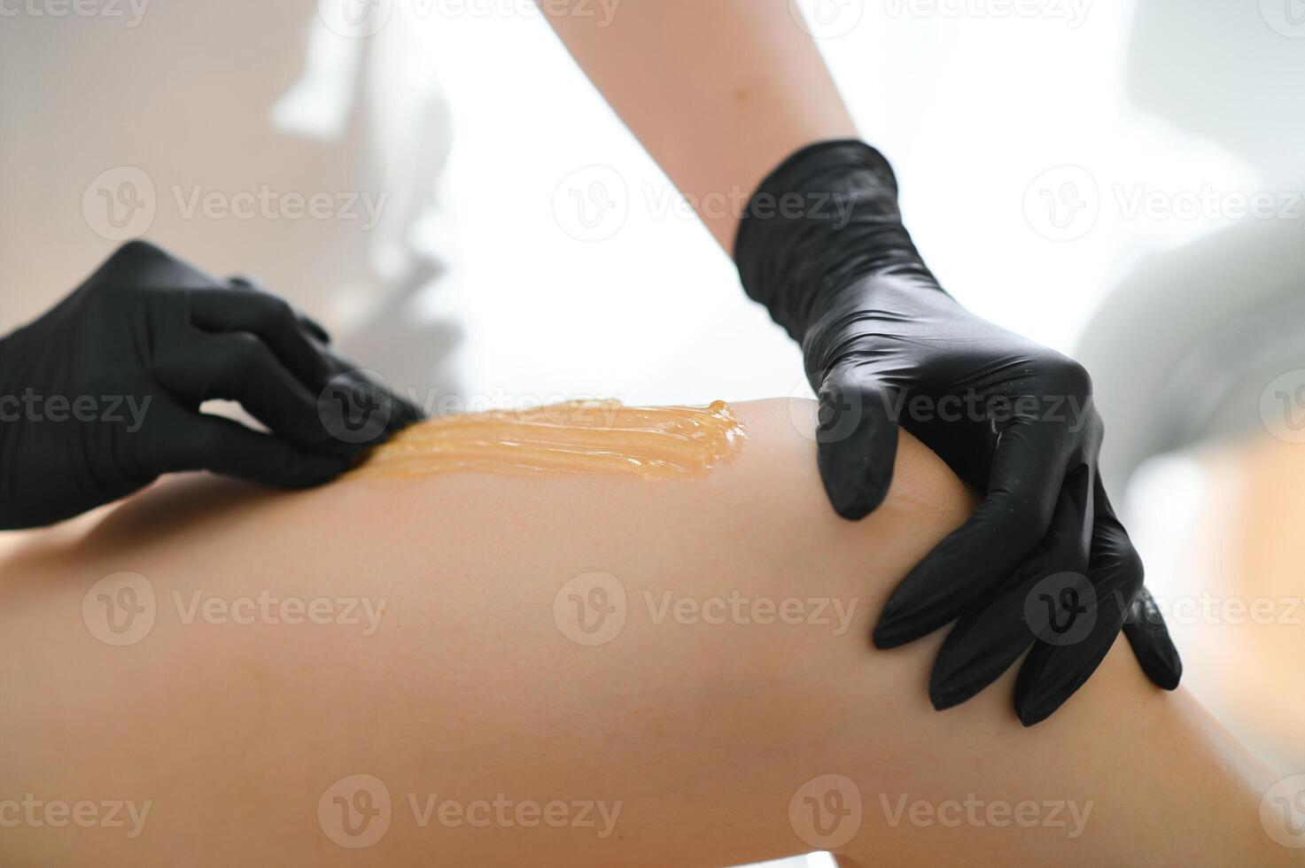 Young woman depilating legs with liquid sugar in spa center photo