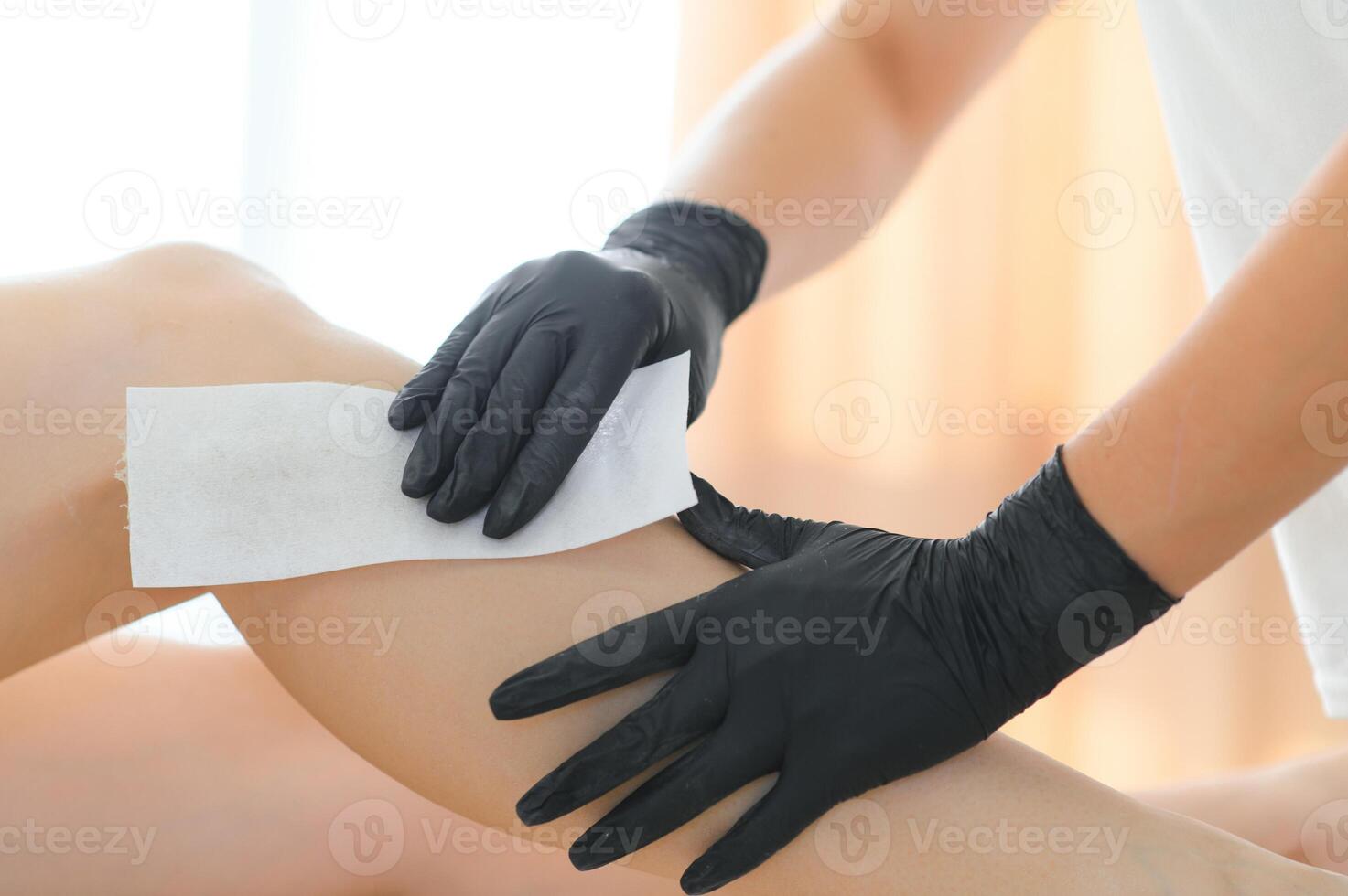 Beautician waxing female legs in spa center photo