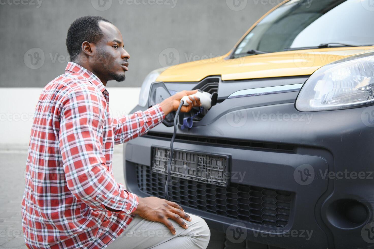 Portrait of a young african man standing with charging cable near the charging station. photo