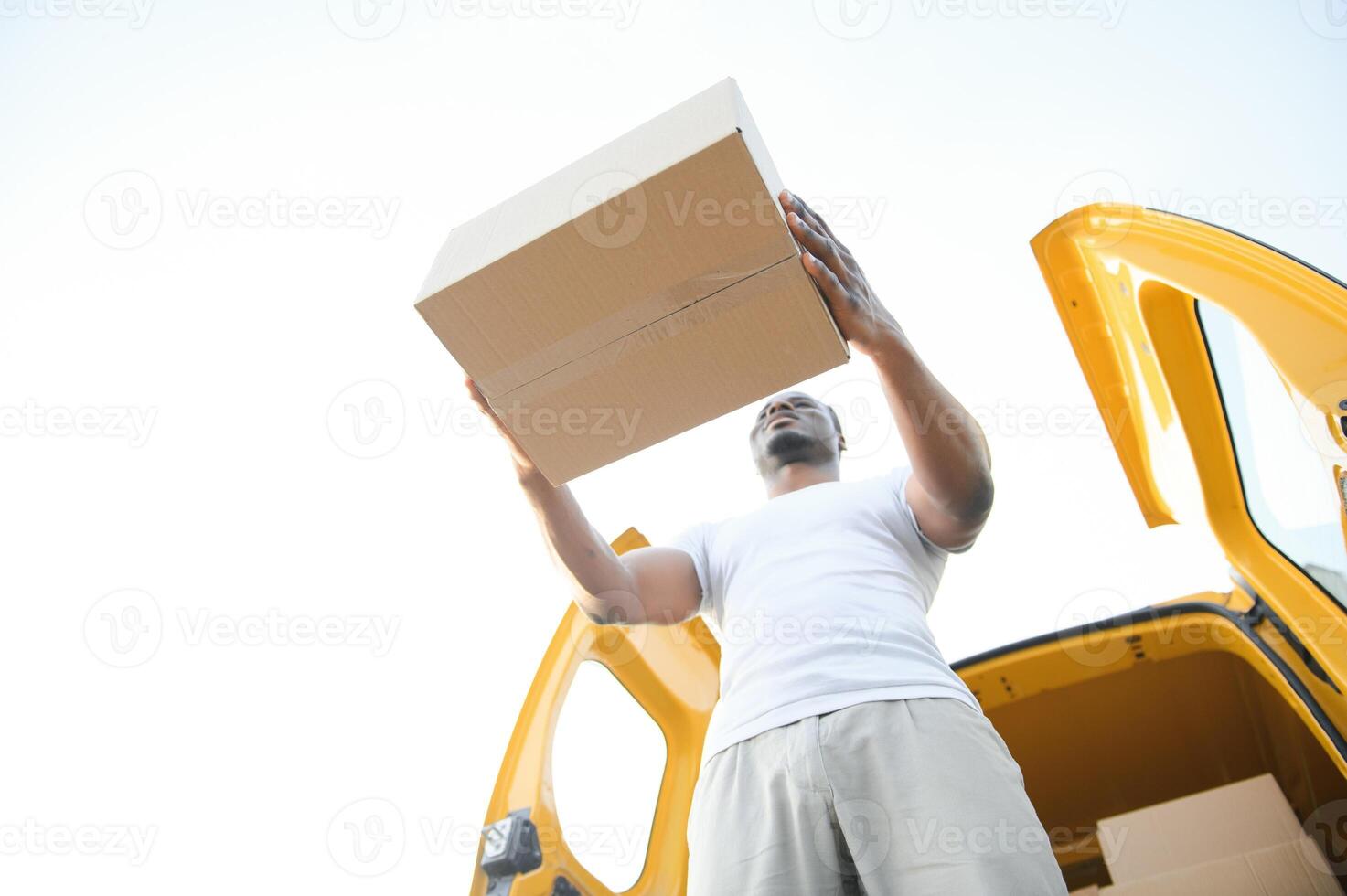 Low Angle View Of Loader Man Standing Near The Van Holding Cardboard Box photo