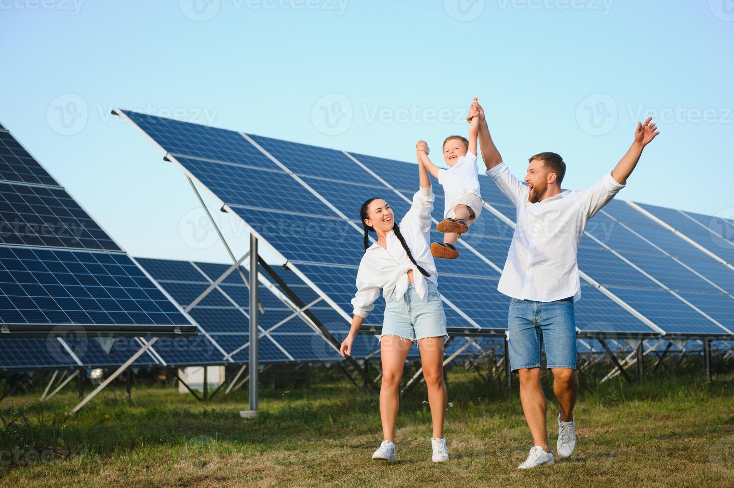 A wide shot of a happy family standing together and smiling at camera with a large solar panel in background photo