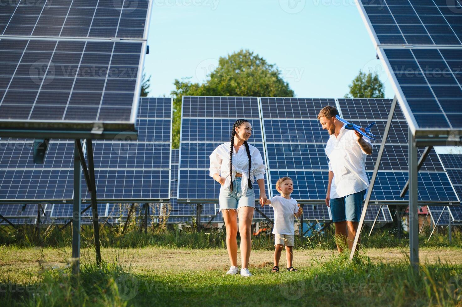 Enthusiastic father showing potential of alternative energy. Contemporary family looking at new solar station they bought. Side view of happy parents and interested child next to solar panels photo