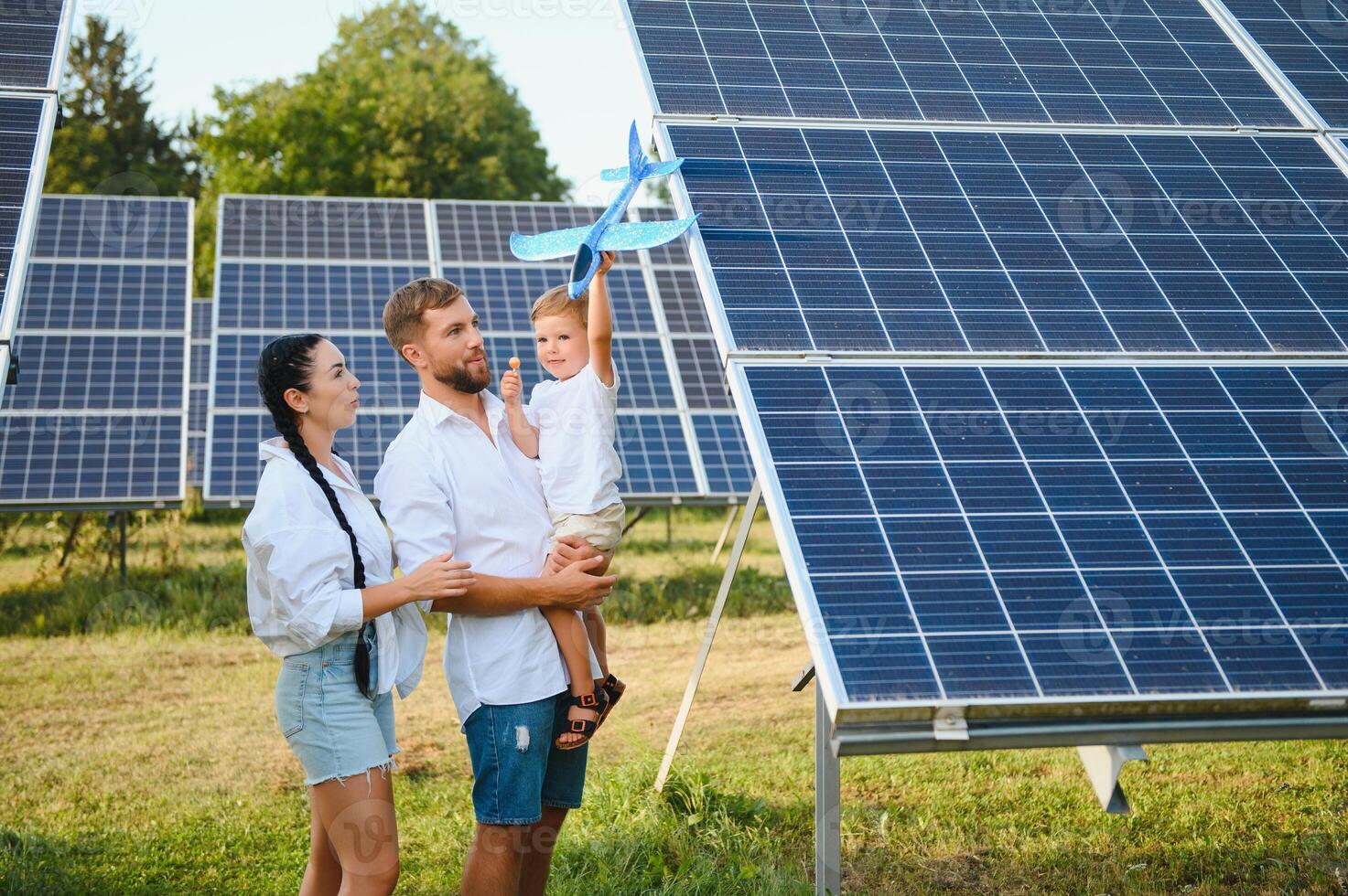 A wide shot of a happy family standing together and smiling at camera with a large solar panel in background photo