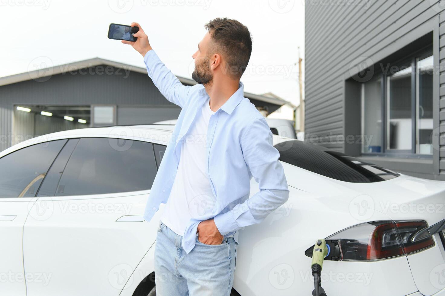 hermosa joven elegante hombre es con eléctrico coche a tiempo de día cargando el vehículo foto