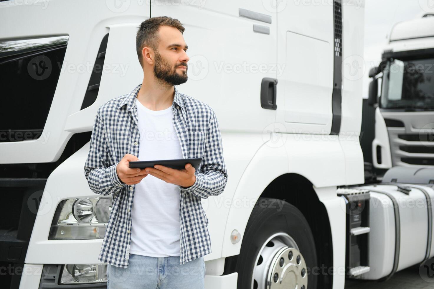 Portrait of young bearded trucker standing by his truck vehicle. Transportation service. Truck driver job photo