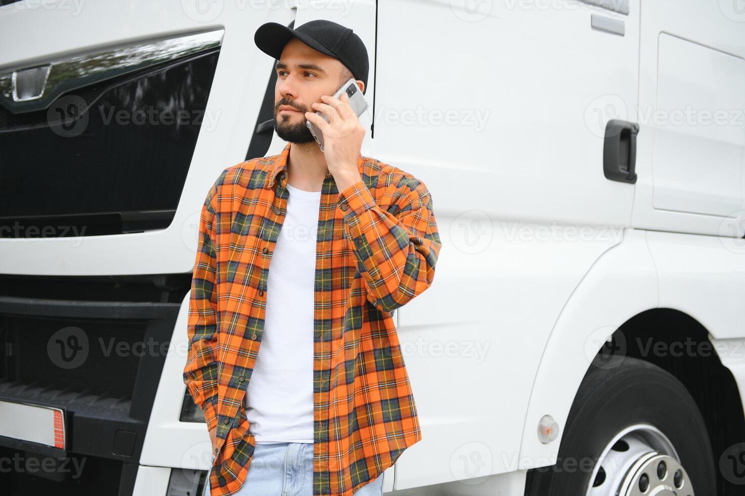 Portrait of young bearded man standing by his truck. Professional truck driver standing by semi truck vehicle. photo