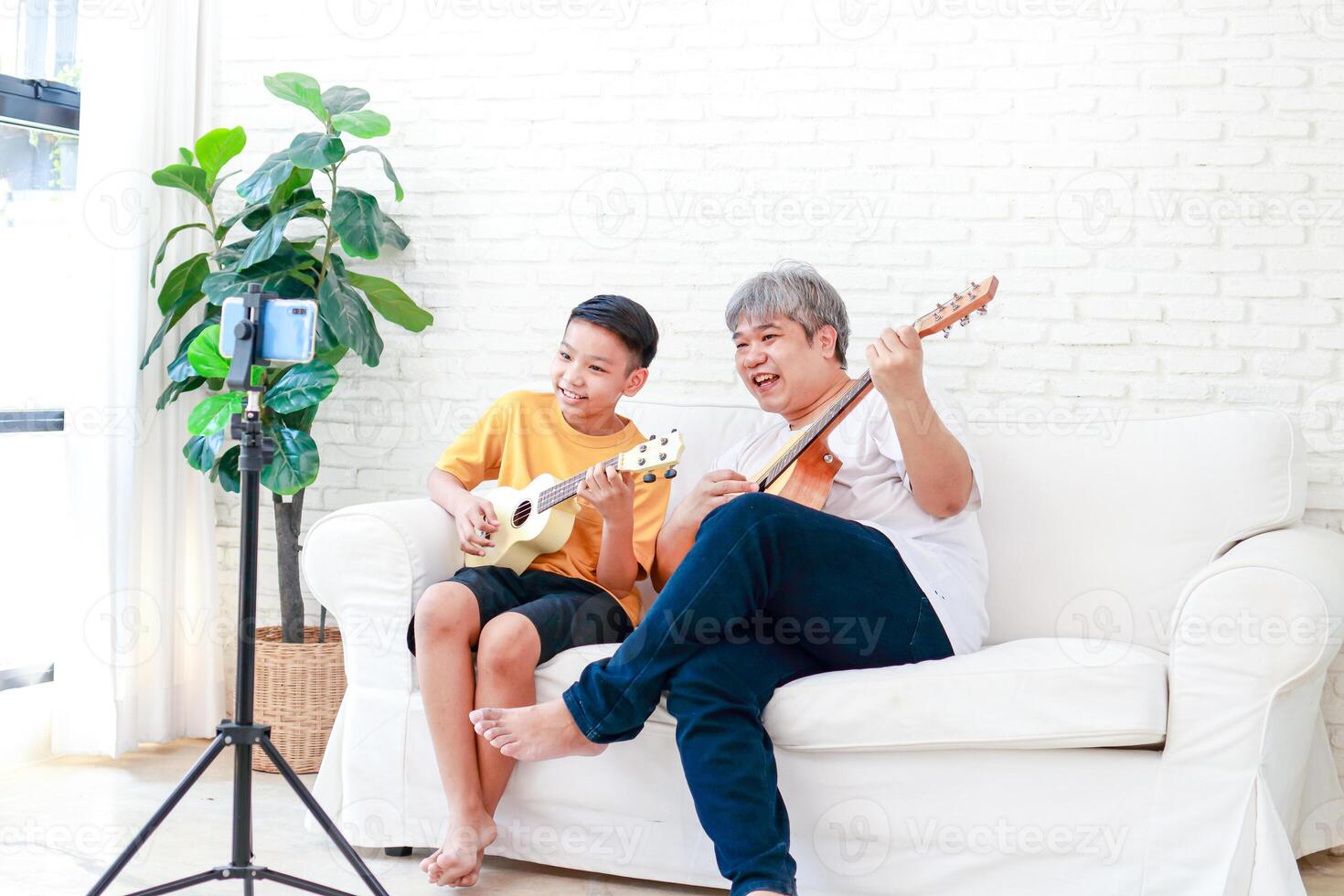 Asian father and son playing music together at home They are happy with the music. Learn music online through your smartphone. leisure activities. modern communication new lifestyle photo
