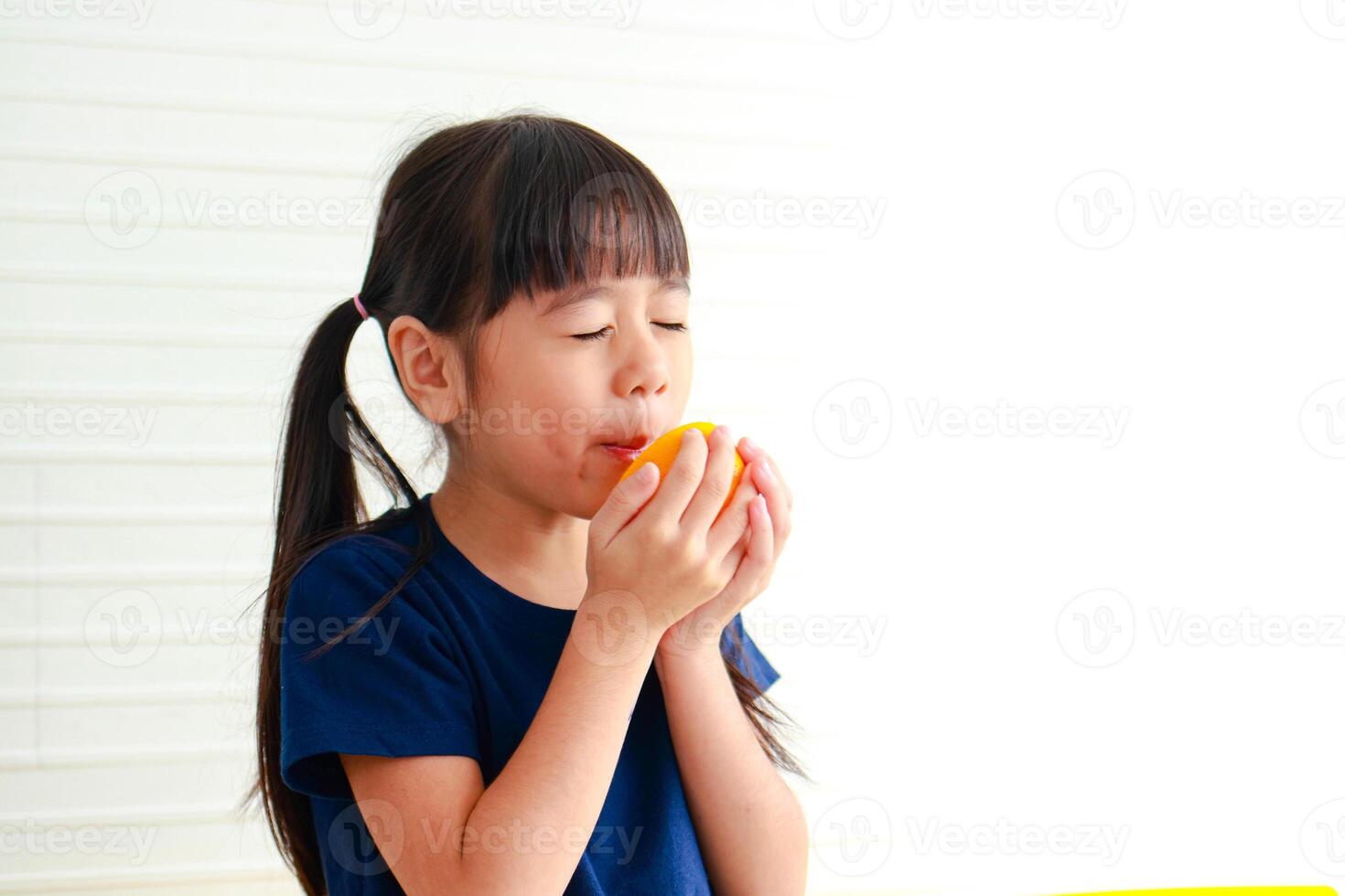 nutrición para edad escolar niños. linda pequeño asiático niña disfruta comiendo naranjas elegir el Derecha comida según a el años de el niño para bueno salud foto