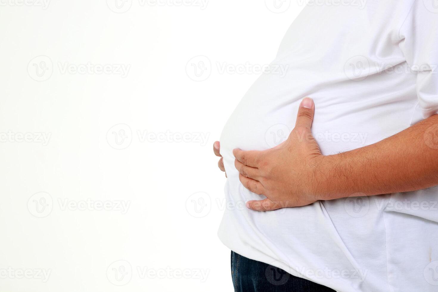 un grasa asiático hombre en un blanco camiseta destacado participación su barriga. él sintió incómodo, abdominal distensión, y tenido síntomas de enfermedad. peso pérdida concepto. salud cuidado. blanco antecedentes. Copiar espacio foto