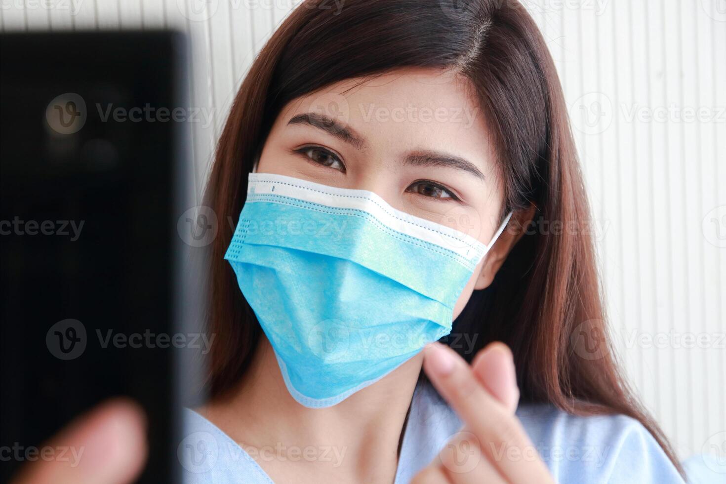 Asian female patient wearing mask in hospital patient room She holds a smartphone online talking to her family. Concept of medical services. patients infected with coronavirus photo