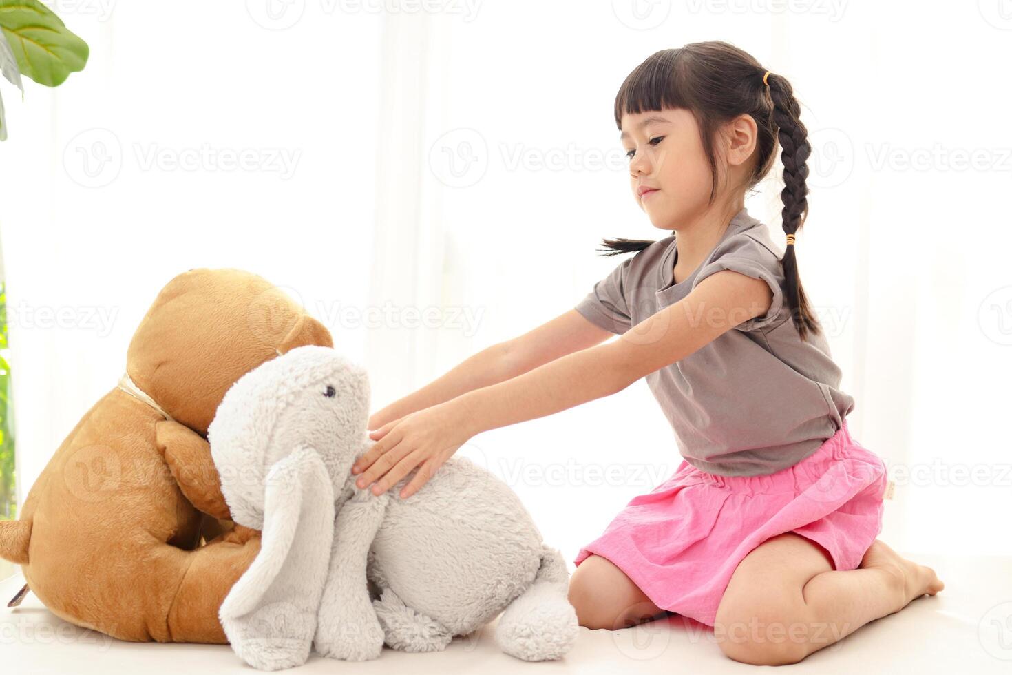 cute little asian girl having fun She sits with a teddy bear and a big rabbit on the white bed. concept of family, friendship photo