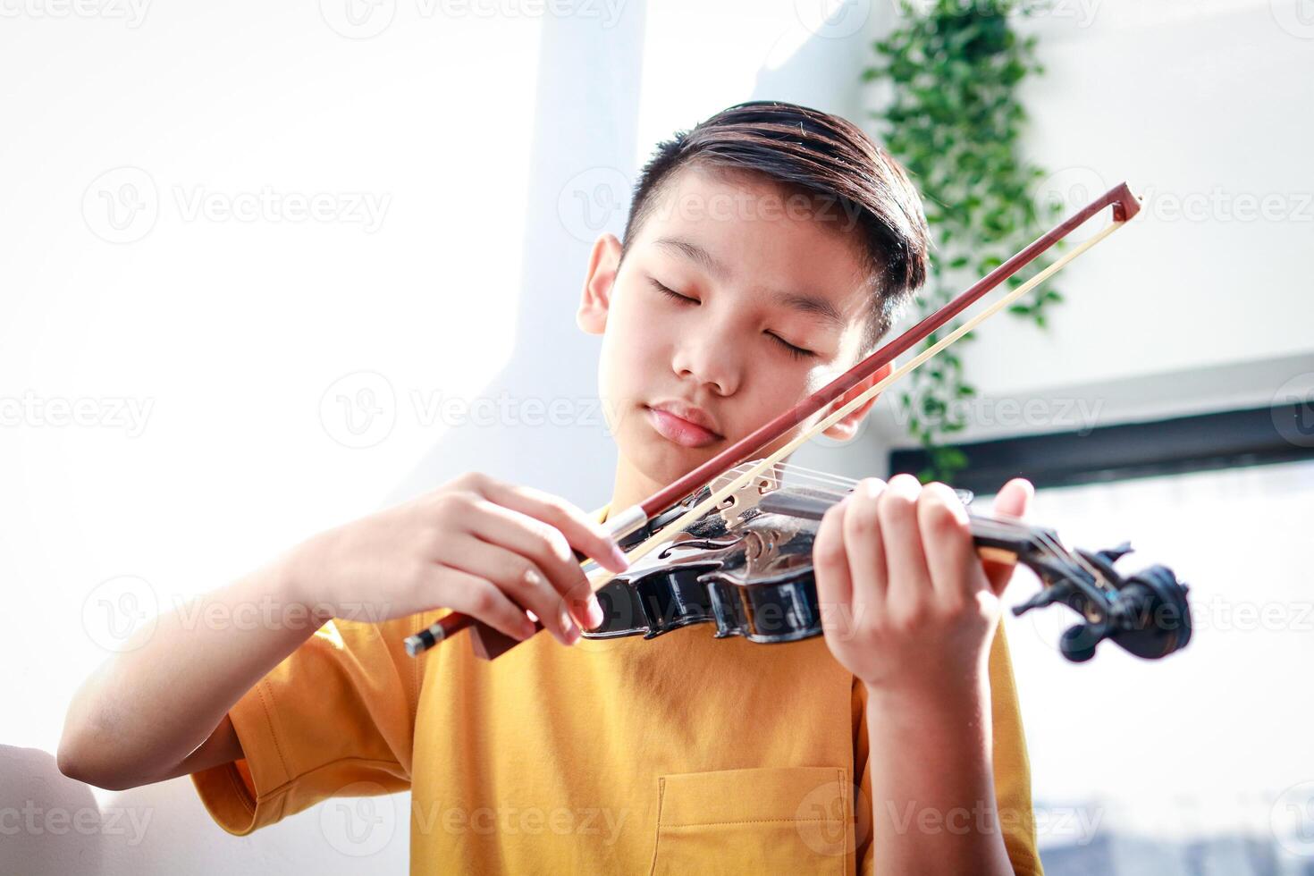 An Asian boy sits at home in the morning playing music. He was happily playing the violin of a classical instrument. Classical music concepts, develop learning, study and practice in childhood. photo