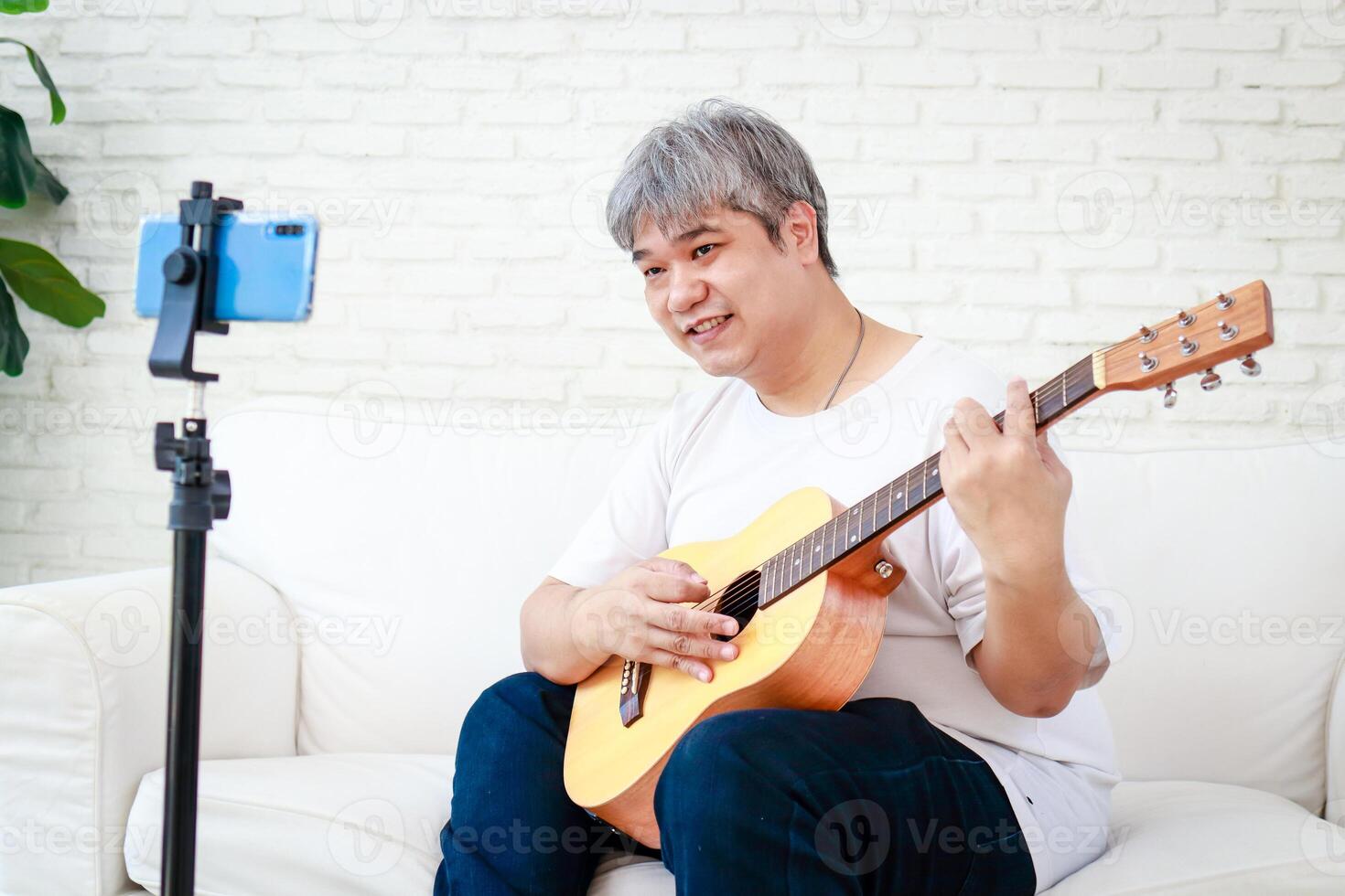 Asian white haired man playing music at home enjoying the music. Learn music online through your smartphone. leisure activities. modern communication new lifestyle photo