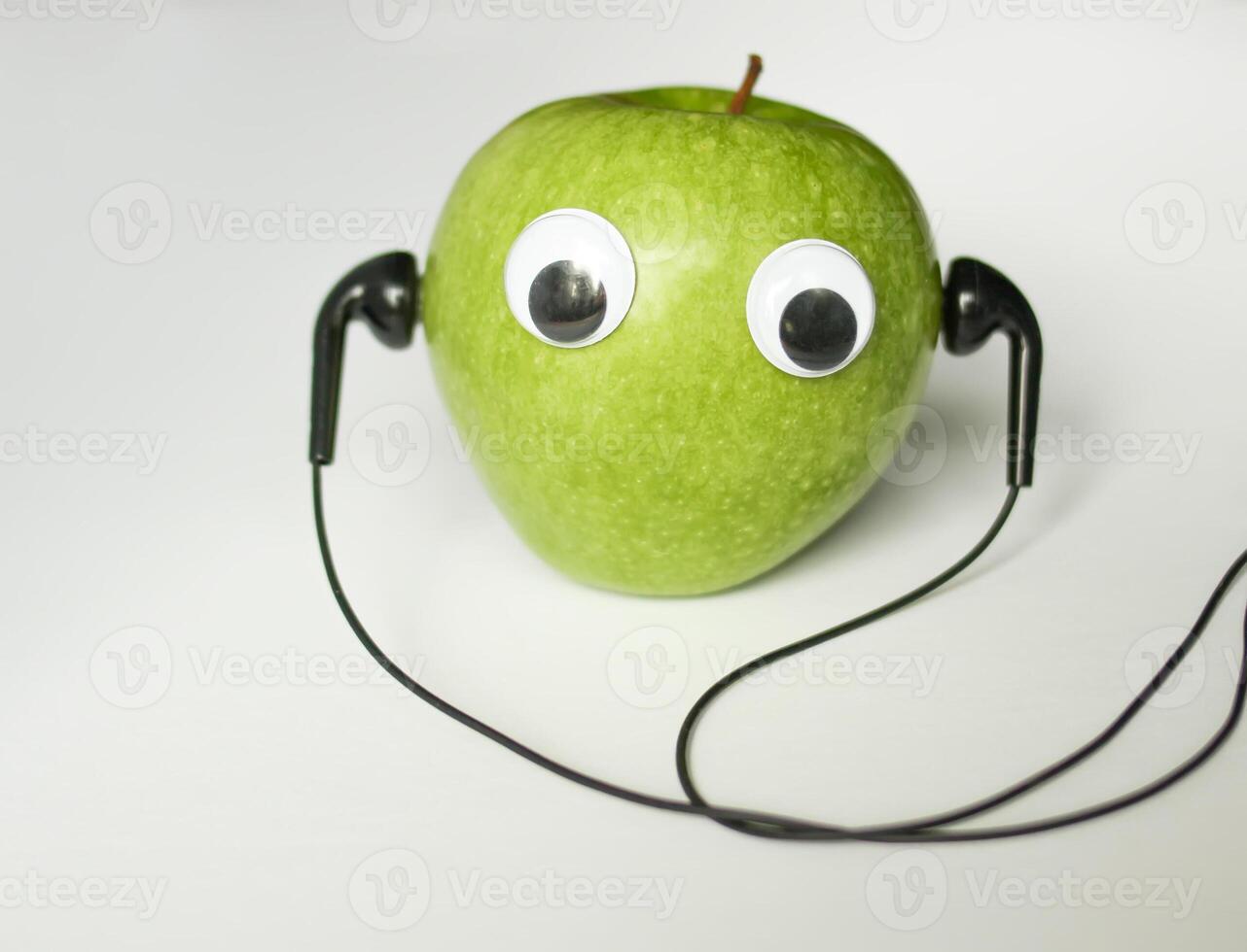 verde pequeño manzana con linda ojos y auriculares en blanco antecedentes. conceptual foto. foto