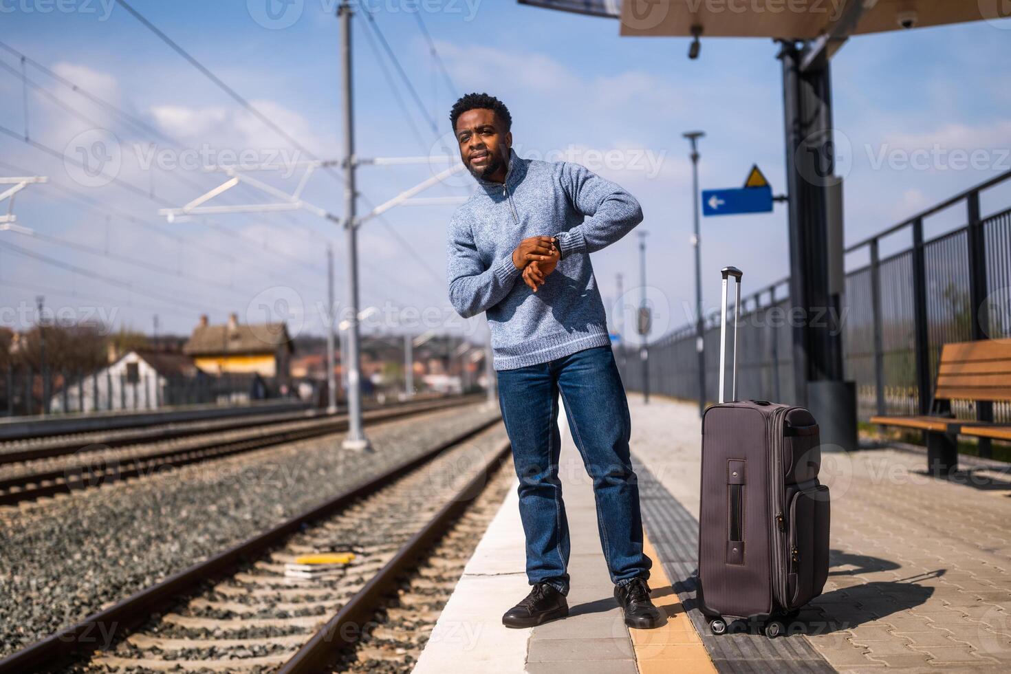 Worried man looking at his clock while standing with suitcase on a railway station. photo