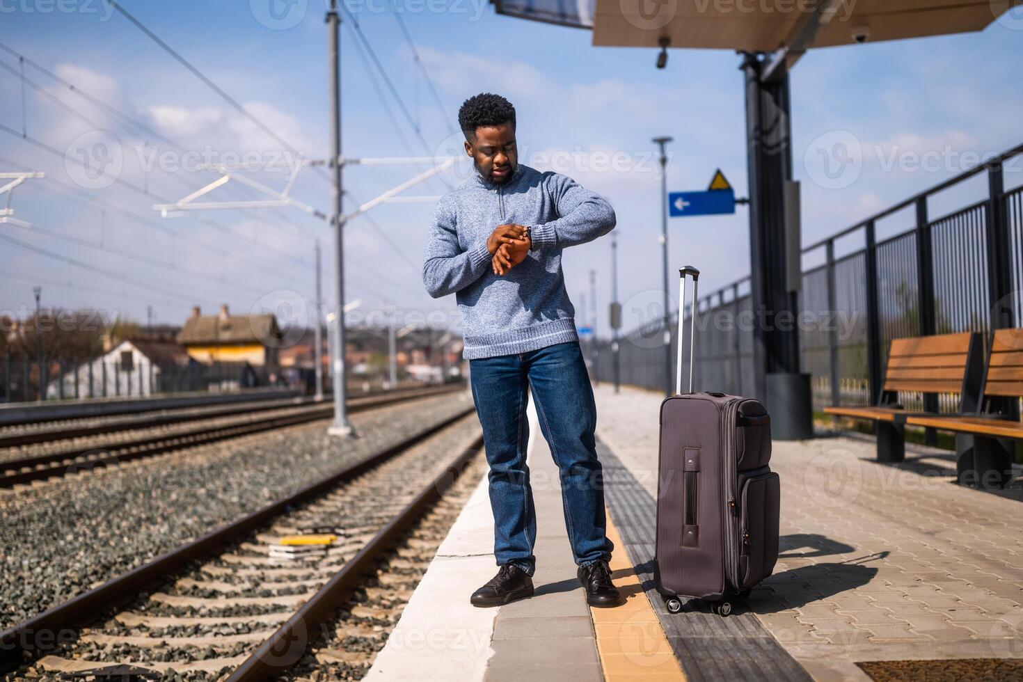 preocupado hombre mirando a su reloj mientras en pie con maleta en un ferrocarril estación. foto