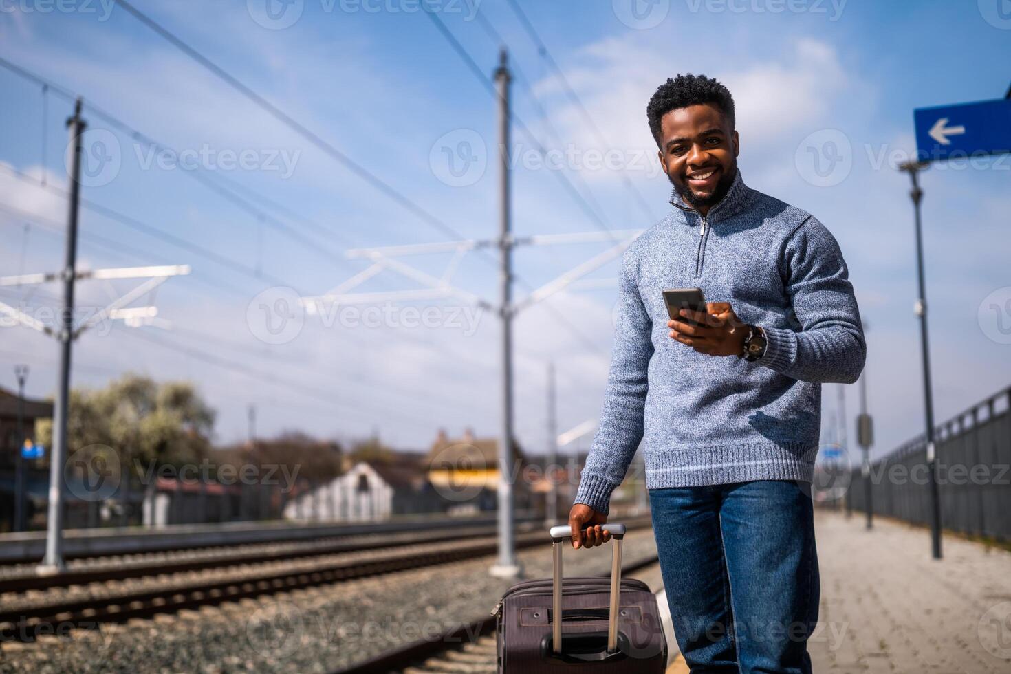 contento hombre con un maleta utilizando teléfono mientras en pie en el ferrocarril estación foto