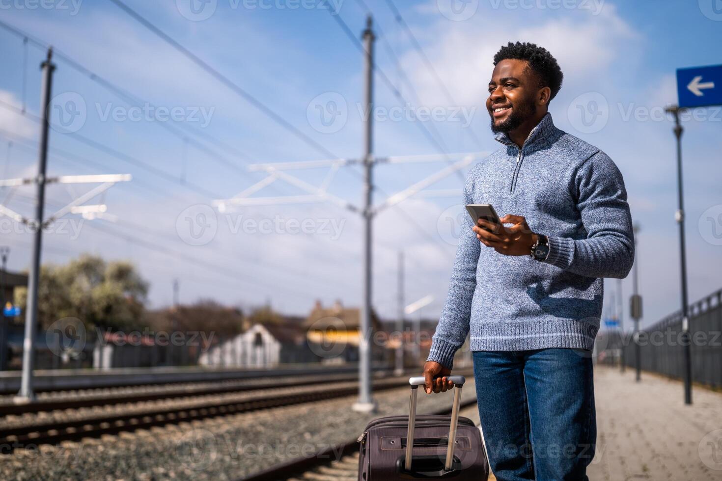 contento hombre con un maleta utilizando teléfono mientras en pie en el ferrocarril estación foto