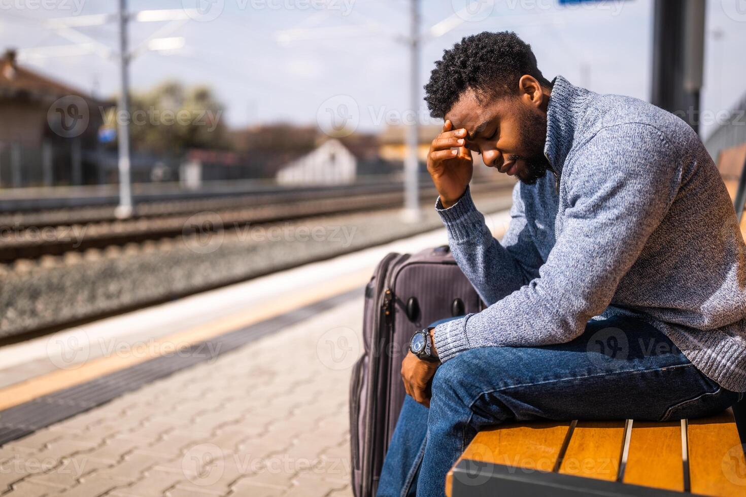 Worried man with a suitcase sitting on a bench at the railway station. photo