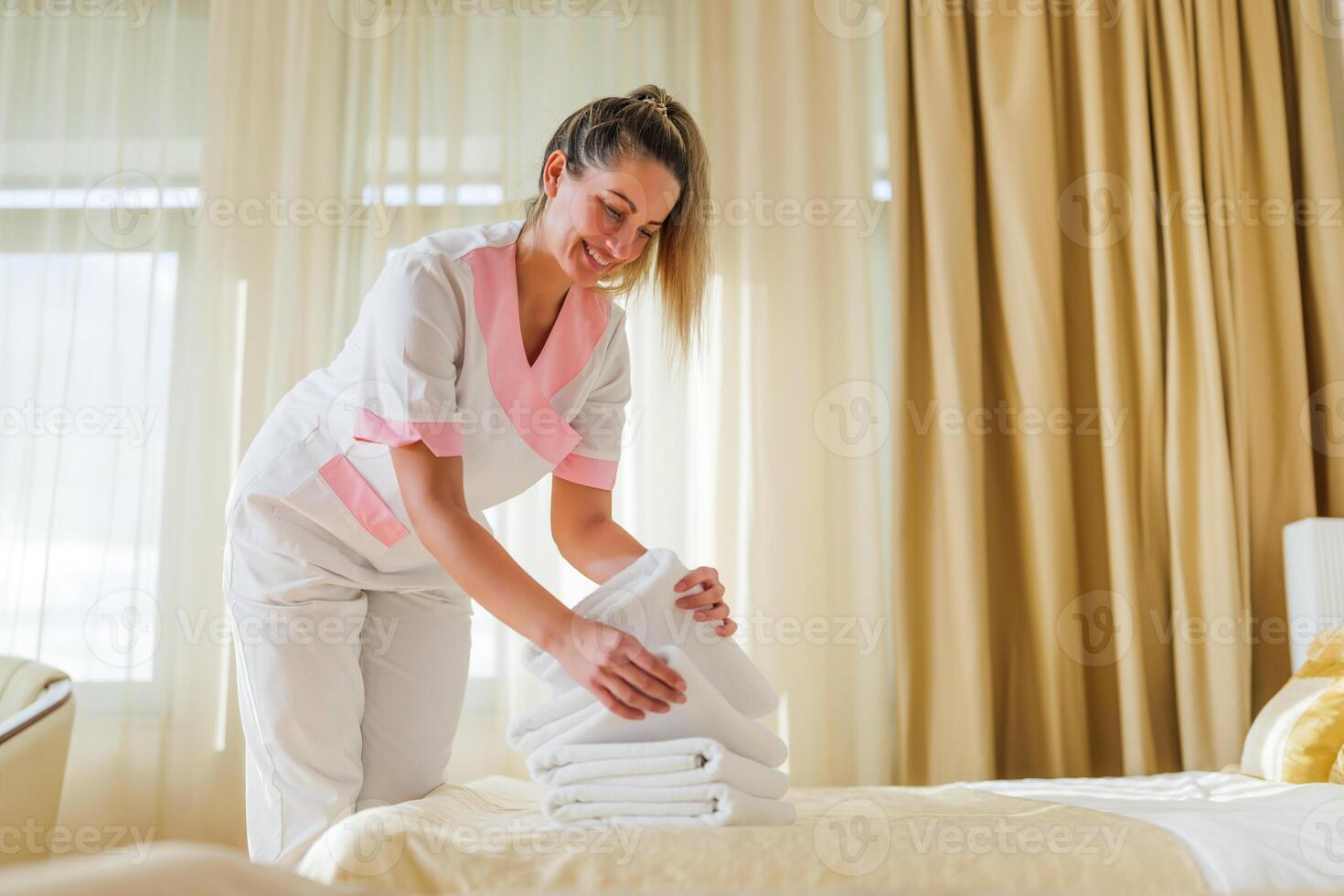 Beautiful hotel maid putting fresh and clean towels on bed in room. photo