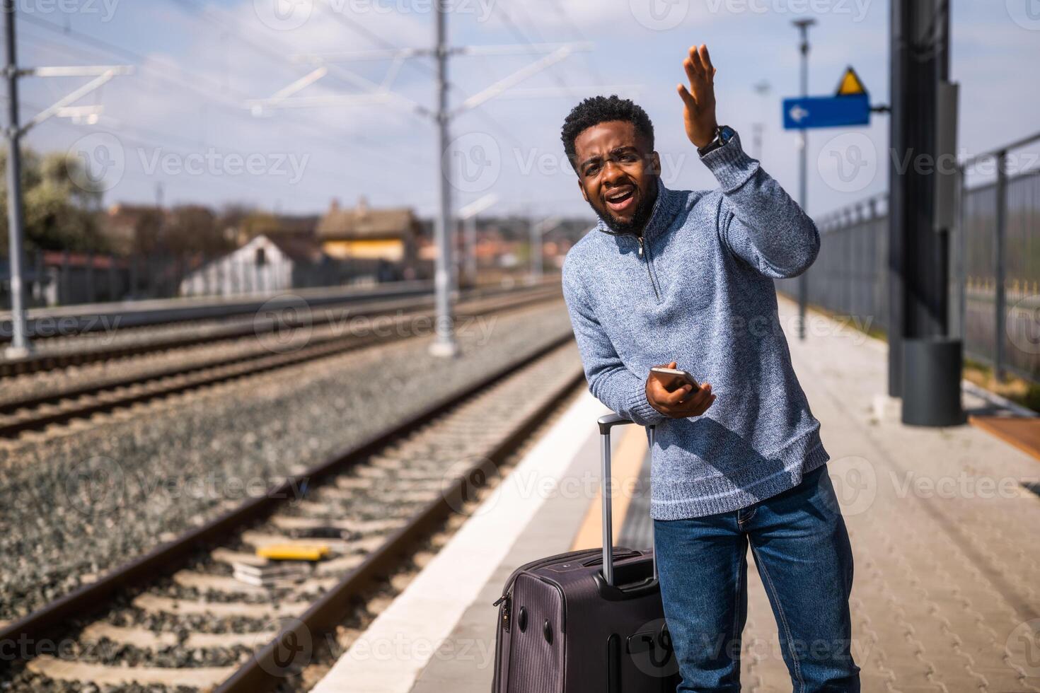 enojado hombre con un maleta y móvil teléfono en pie en un ferrocarril estación. foto