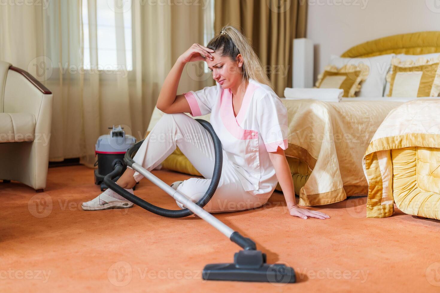 Image of sad overworked hotel maid sitting on the floor in a room. photo