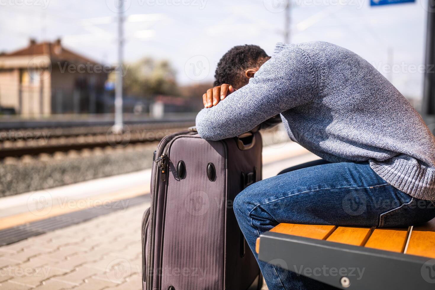 Worried man with a suitcase sitting on a bench at the railway station. photo