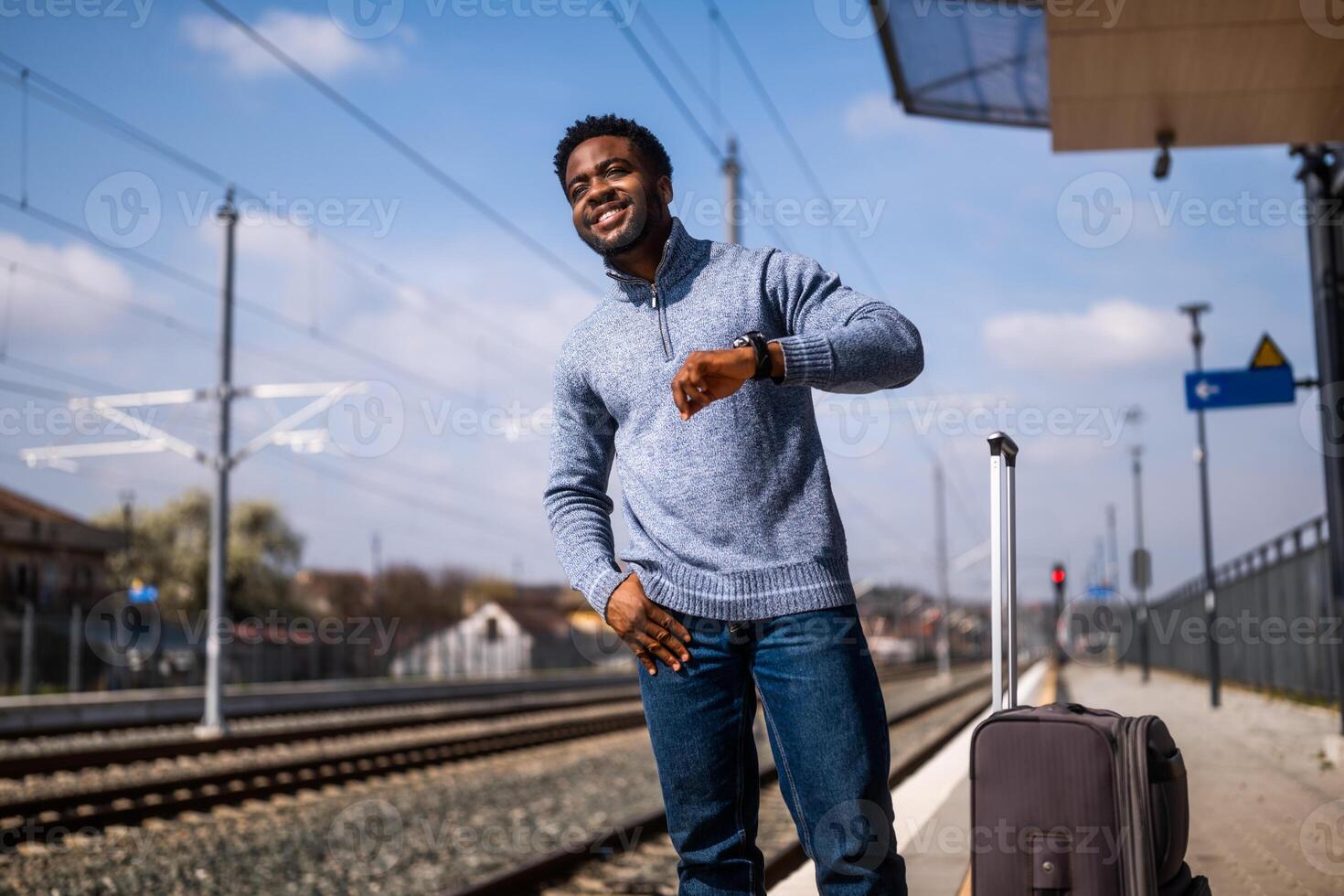 contento hombre mirando a su reloj mientras en pie con maleta en un ferrocarril estación. foto