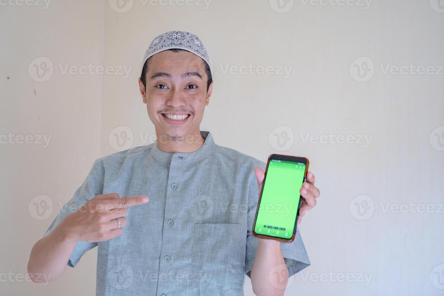 musulmán asiático hombre feliz, sonriente cuando espectáculo el teléfono inteligente con verde pantalla cuando Ramadán celebracion. el foto es adecuado a utilizar para ramadhan póster y musulmán contenido medios de comunicación.