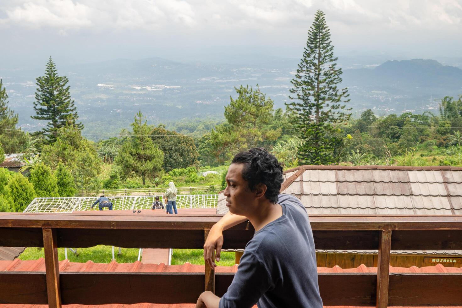 Man sitting near fence and looking the landscape mountain. The photo is suitable to use for calm enjoyed activity, leisure activity and park background.