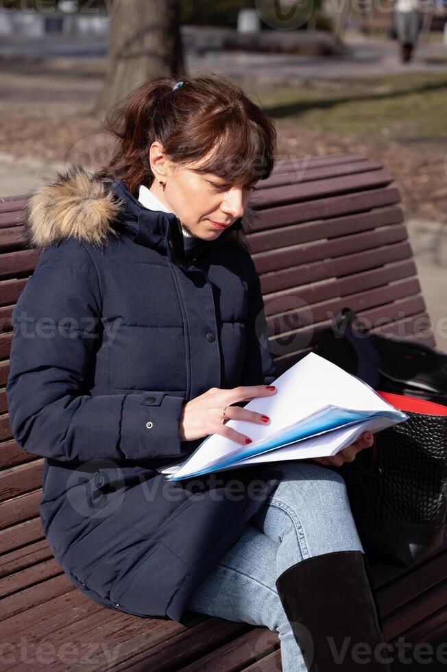 A young female accountant sits on a park bench and looks through reporting documents during her break photo