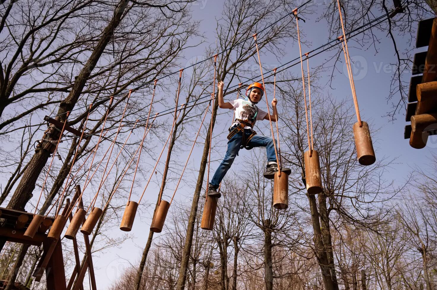 A boy in a helmet climbs a rope park in the spring photo