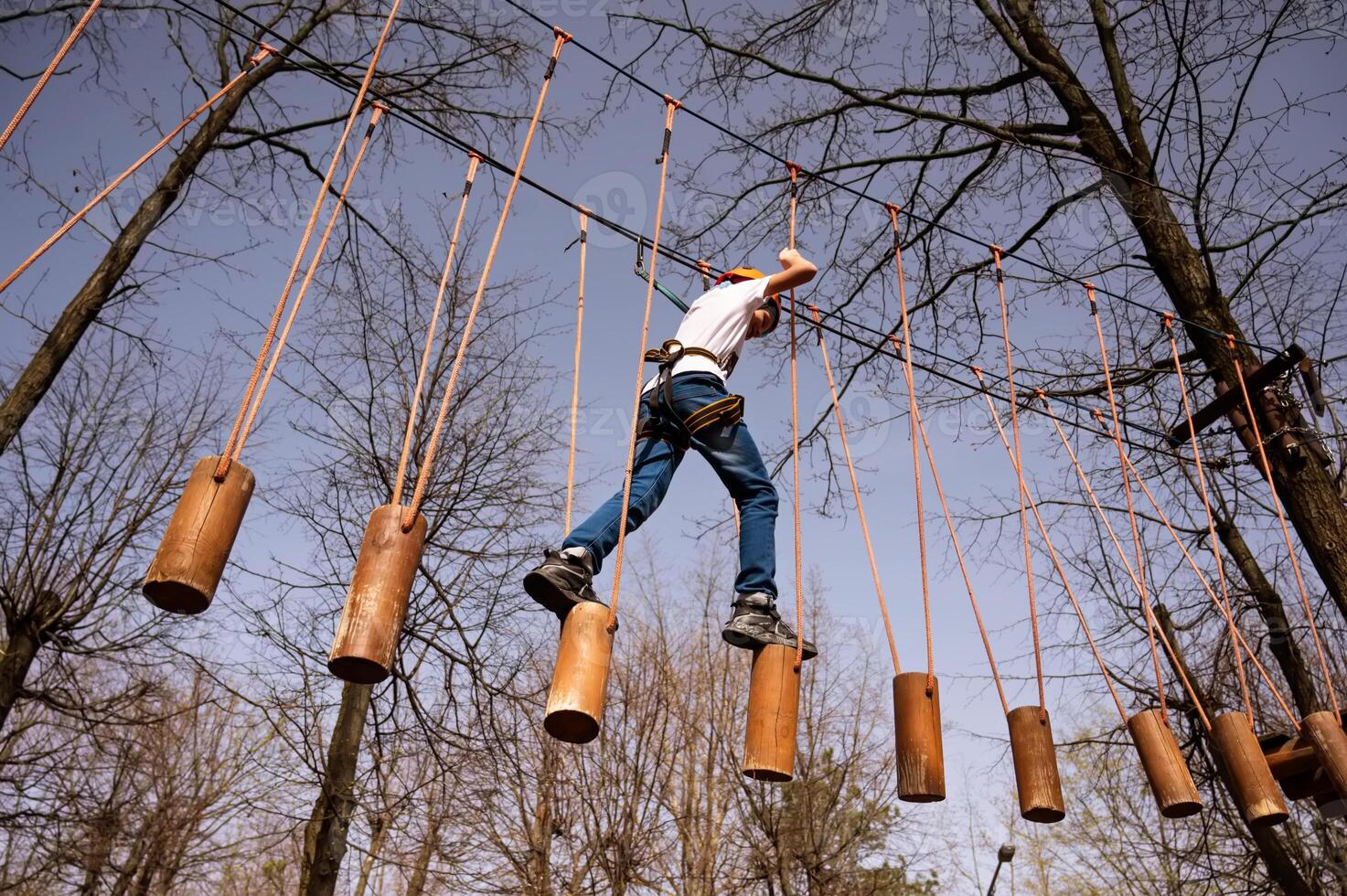 A boy in a helmet climbs a rope park in the spring photo