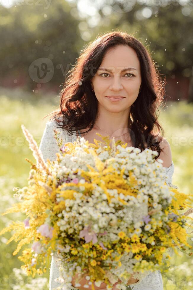Portrait of a dark-haired girl with a large bouquet of wildflowers. photo