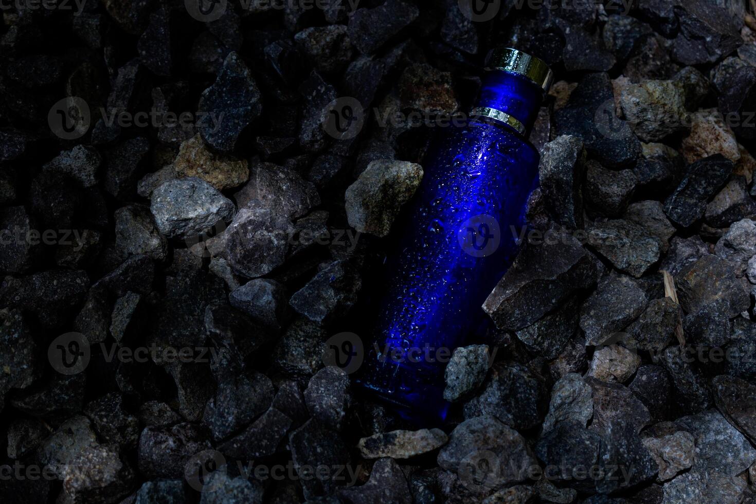 Perfume Dark Blue transparent bottle in gravel or coral background photo