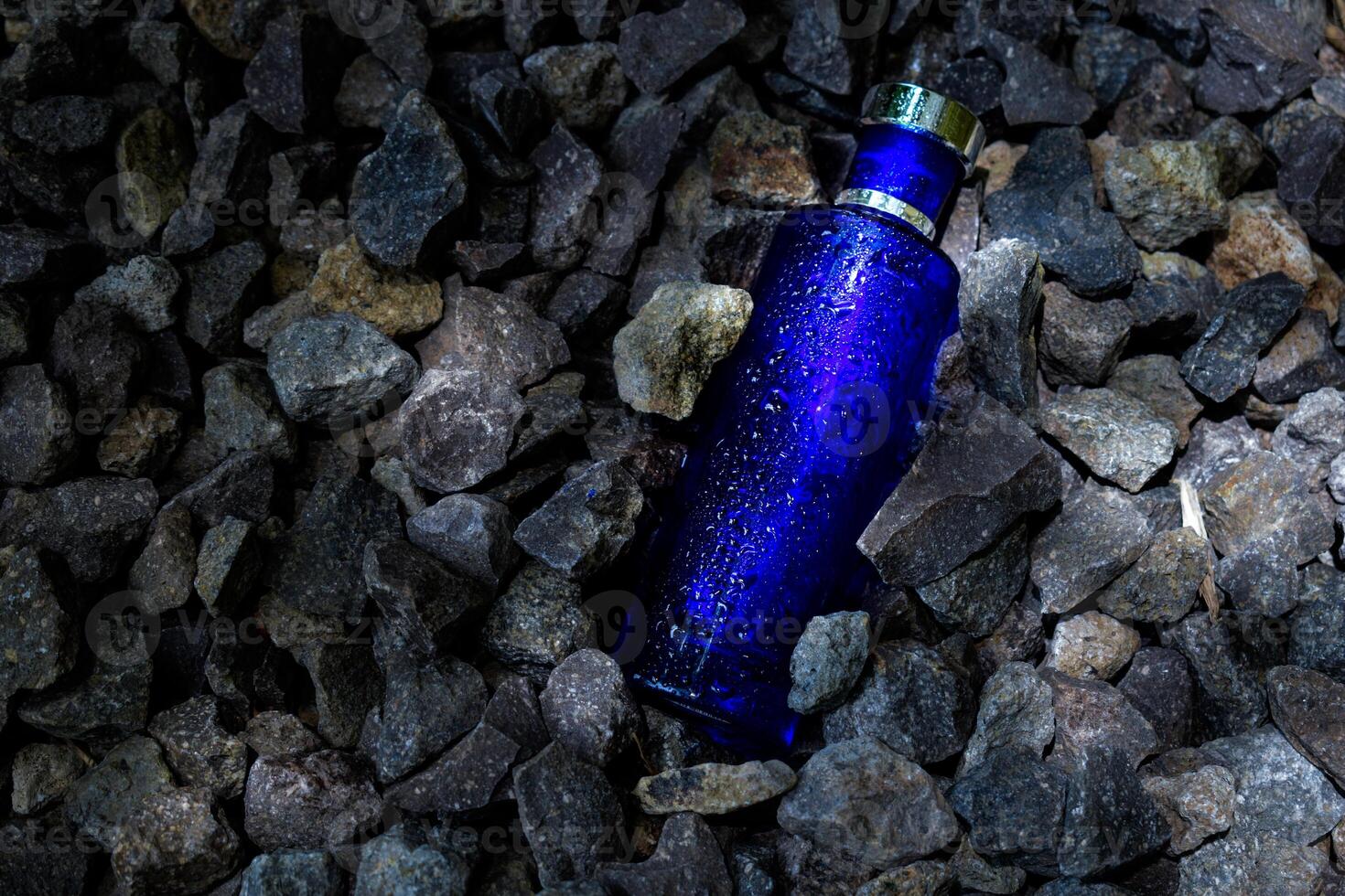 Perfume Dark Blue transparent bottle in gravel or coral background photo