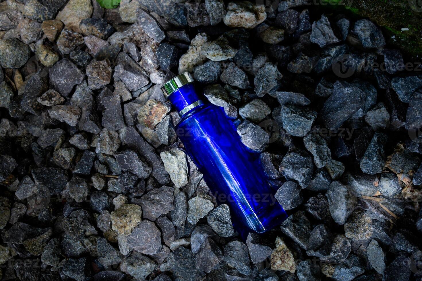 Perfume Dark Blue transparent bottle in gravel or coral background photo