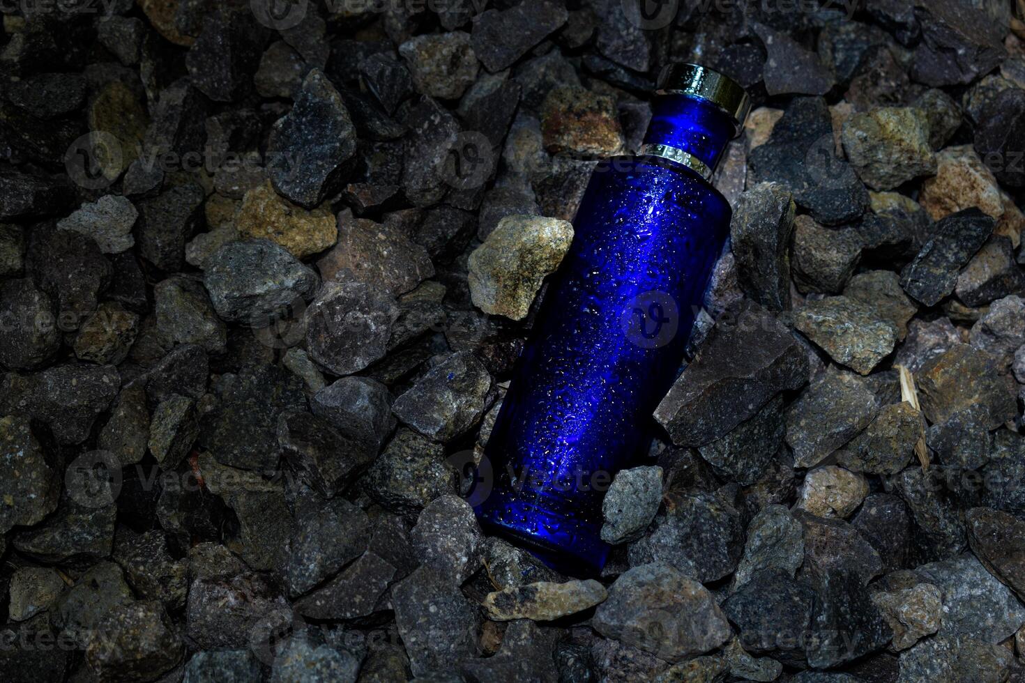 Perfume Dark Blue transparent bottle in gravel or coral background photo