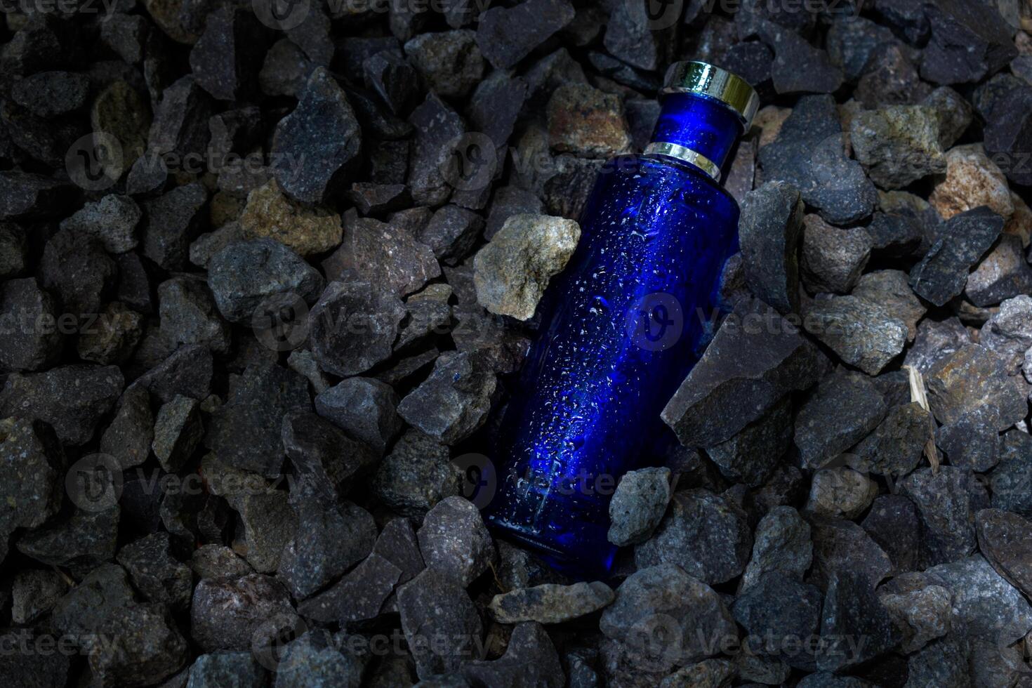 Perfume Dark Blue transparent bottle in gravel or coral background photo