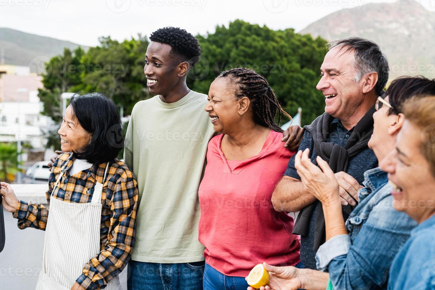 Happy multigenerational friends having fun preparing food at house rooftop - Diversity people lifestyle photo