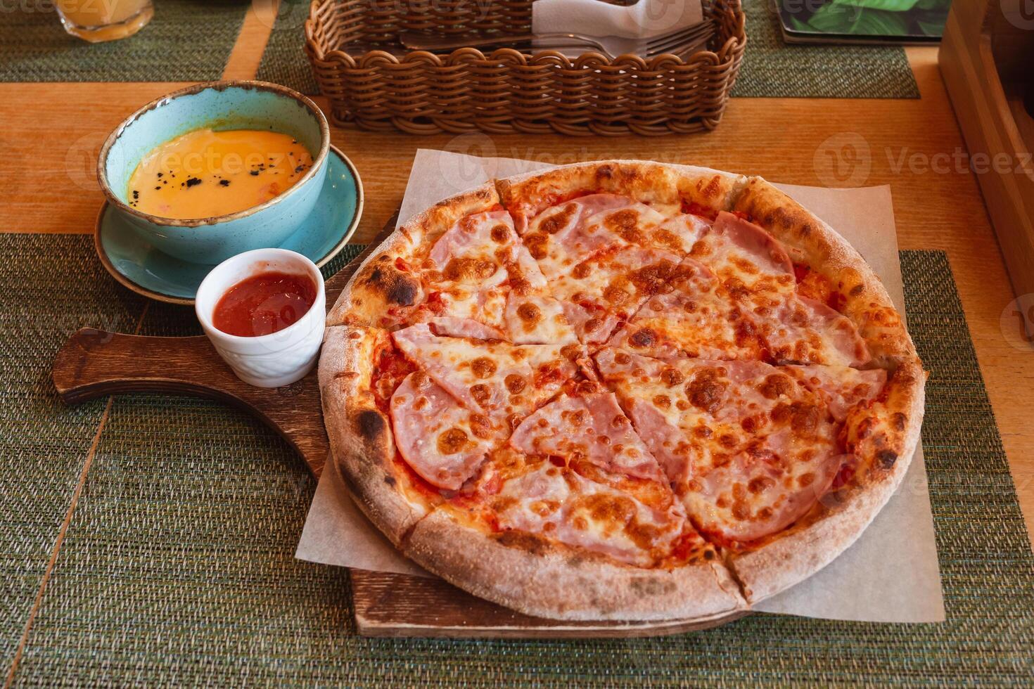 Pizza with ham cut into pieces, lying on the board. Pumpkin cream soup with salmon photo