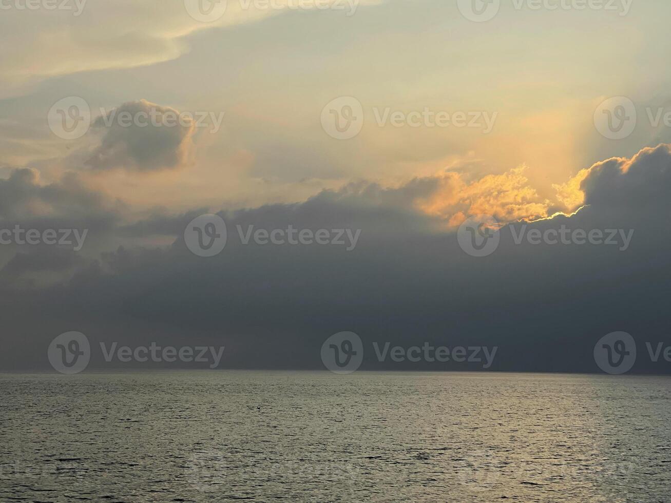 hermosa puesta de sol en el mar, el Dom conjuntos detrás un grande nube acostado en el agua foto