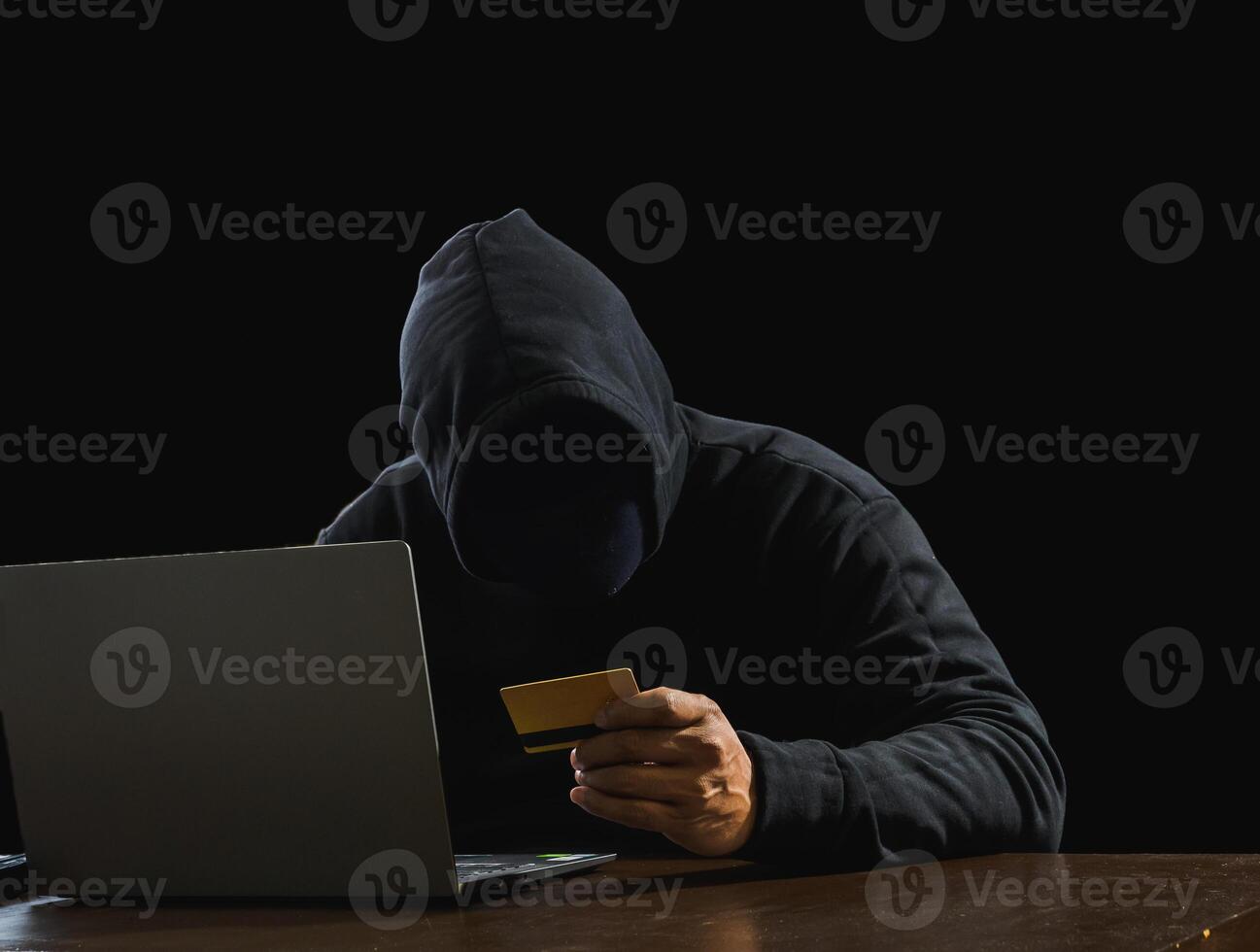 Portrait hacker spy man one person in black hoodie sitting on table looking computer laptop used login password attack security to data digital internet network system night dark background copy space photo