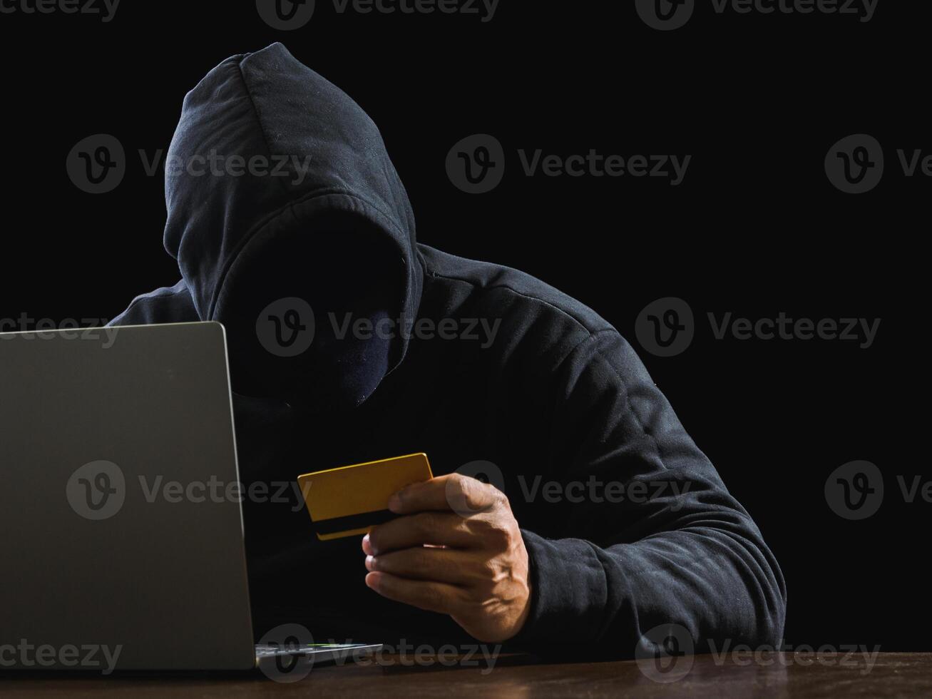 Portrait hacker spy man one person in black hoodie sitting on table looking computer laptop used login password attack security to data digital internet network system night dark background copy space photo