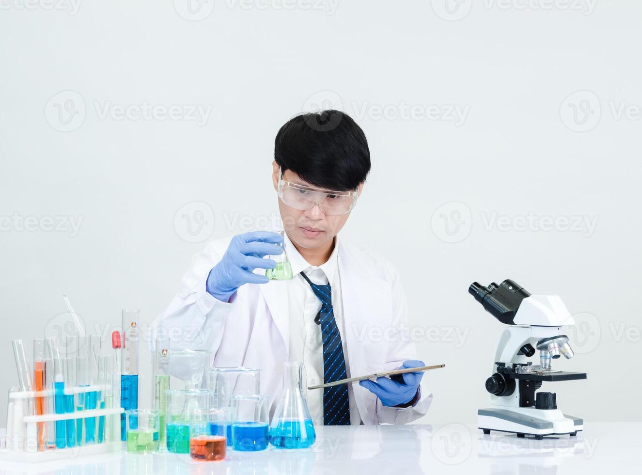 retrato asiático hombre estudiante científico vistiendo un médico vestido en el laboratorio mirando mano a químico. causado por mezcla reactivos en científico investigación laboratorios con prueba tubos y microscopio en el mesa foto