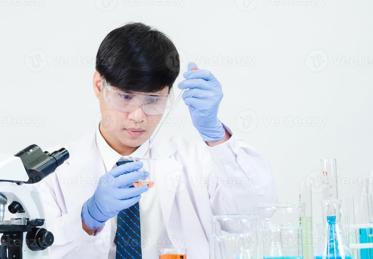 retrato asiático hombre estudiante científico vistiendo un médico vestido en el laboratorio mirando mano a químico. causado por mezcla reactivos en científico investigación laboratorios con prueba tubos y microscopio en el mesa foto